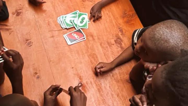 Niños jugando a las cartas alrededor de una mesa de madera, vistos desde arriba